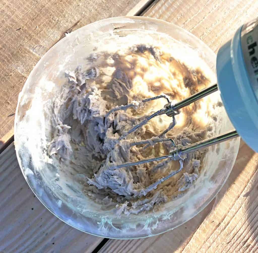 A light blue KitchenAid hand mixer whips diaper rash cream in a glass bowl.