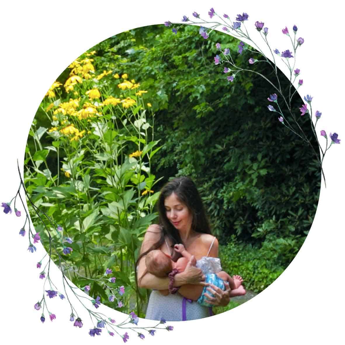 Mother holding baby in front of tall, yellow flowers. Watercolor purple floral border around part of circular image