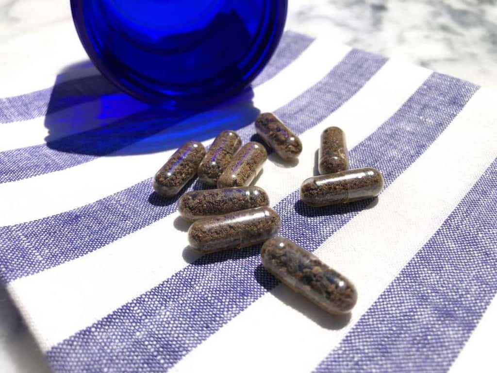 Placenta pills are beside a blue glass bottle on a striped linen napkin on top of a marble table.