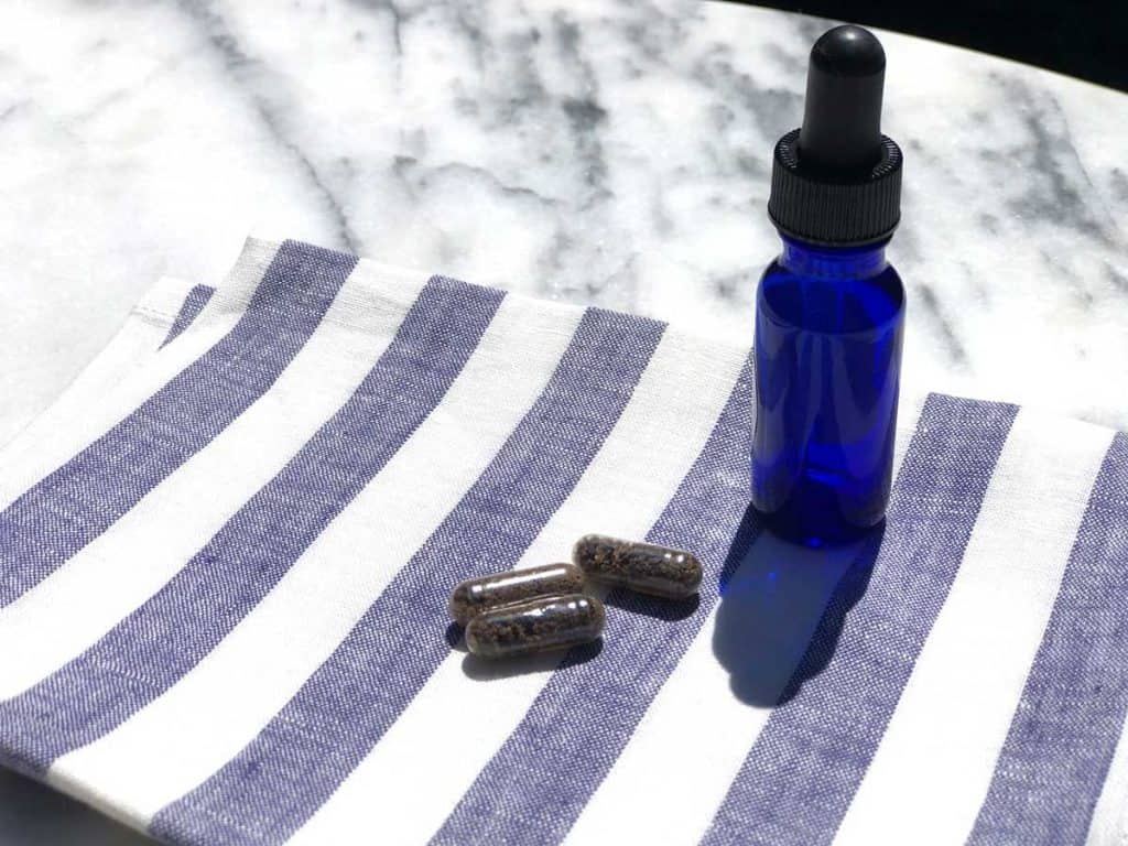 A marble table with a blue glass tincture bottle standing beside three placenta pills on a cloth napkin.