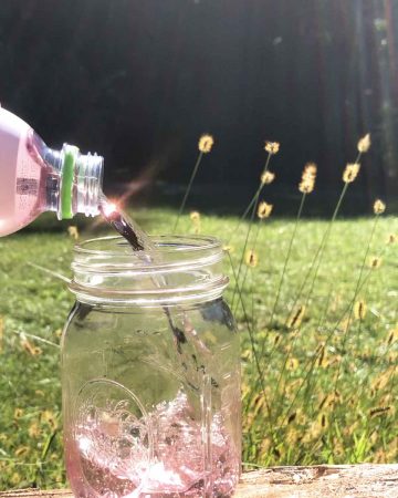Pink coconut water sparkles in the sunlight as it is poured from a bottle.