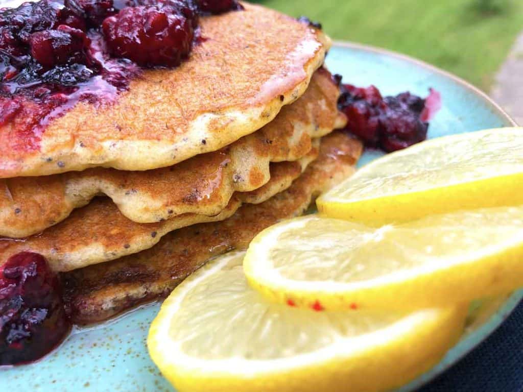 Three lemon slices are on a blue plate in front of a stack of lemon sourdough einkorn sourdough pancakes with berries.