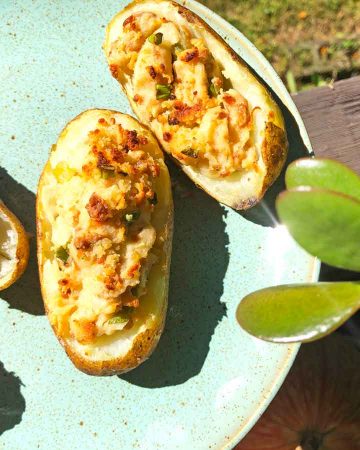 Four plant-based twice baked potatoes are on a blue plate outdoors.