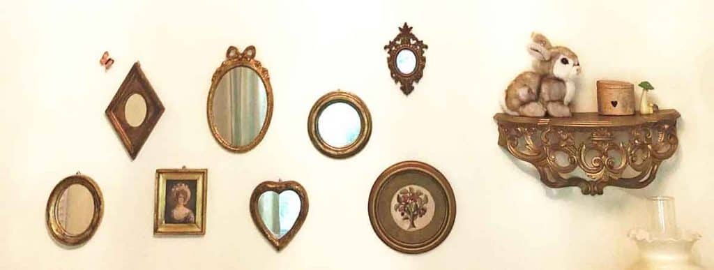 A nursery gallery wall featuring gold mirrors and frames as well as an ornate shelf with a toy rabbit, a wooden box, and a mushroom trinket.