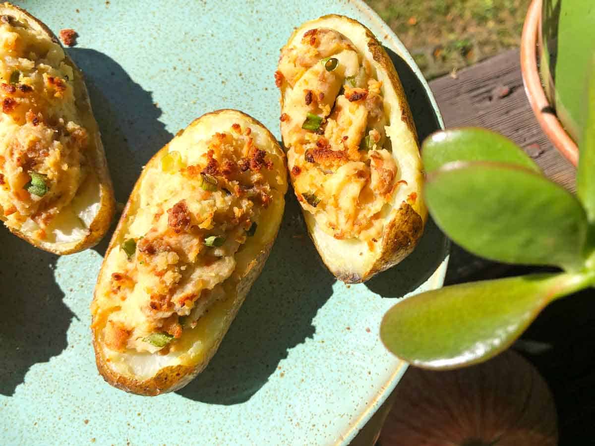Vegan twice baked potatoes are on a blue plate outdoors by a jade plant.