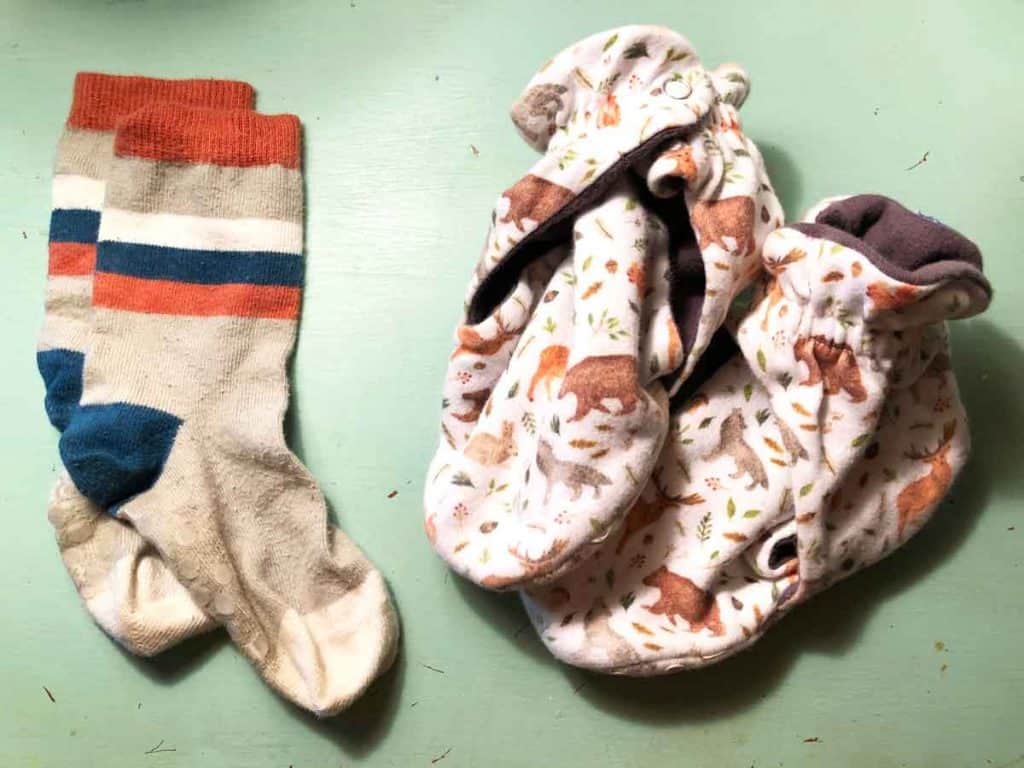 A pair of orange and navy toddler socks is beside a pair of booties with woodland animals on a blue tabletop.
