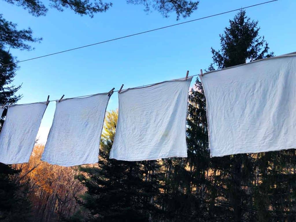 Flat cloth diapers dry on a clothesline outdoors near evergreen trees.