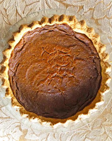 A pumpkin pie with crimped edges rests on a surface with gold leaves.