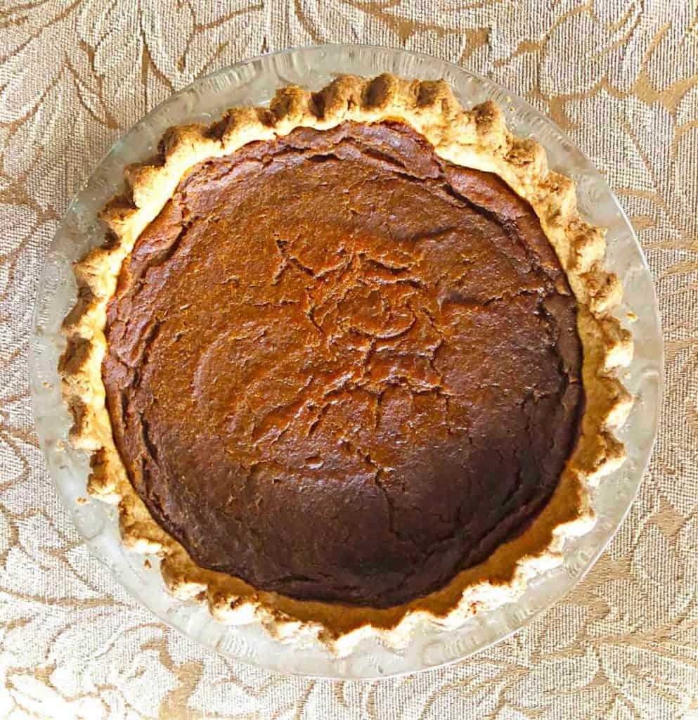 A pumpkin pie with crimped edges rests on a surface with gold leaves.