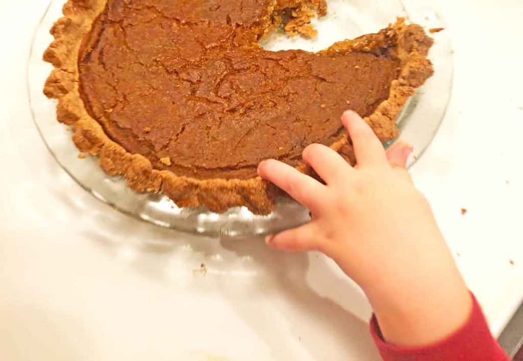 A toddler reaches for a fresh baked pumpkin pie.