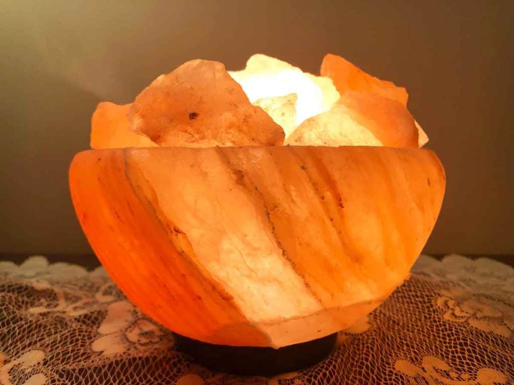 A bowl salt lamp is on top of lace on a wooden surface.