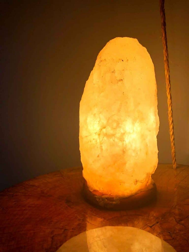 A salt lamp is on a hanging wooden nightstand by a rose quartz coaster.