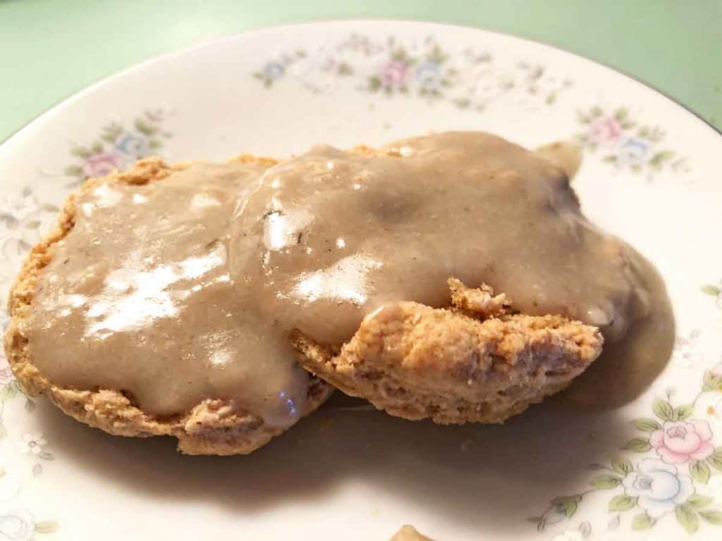 An einkorn biscuit topped with gravy is on a floral dish.