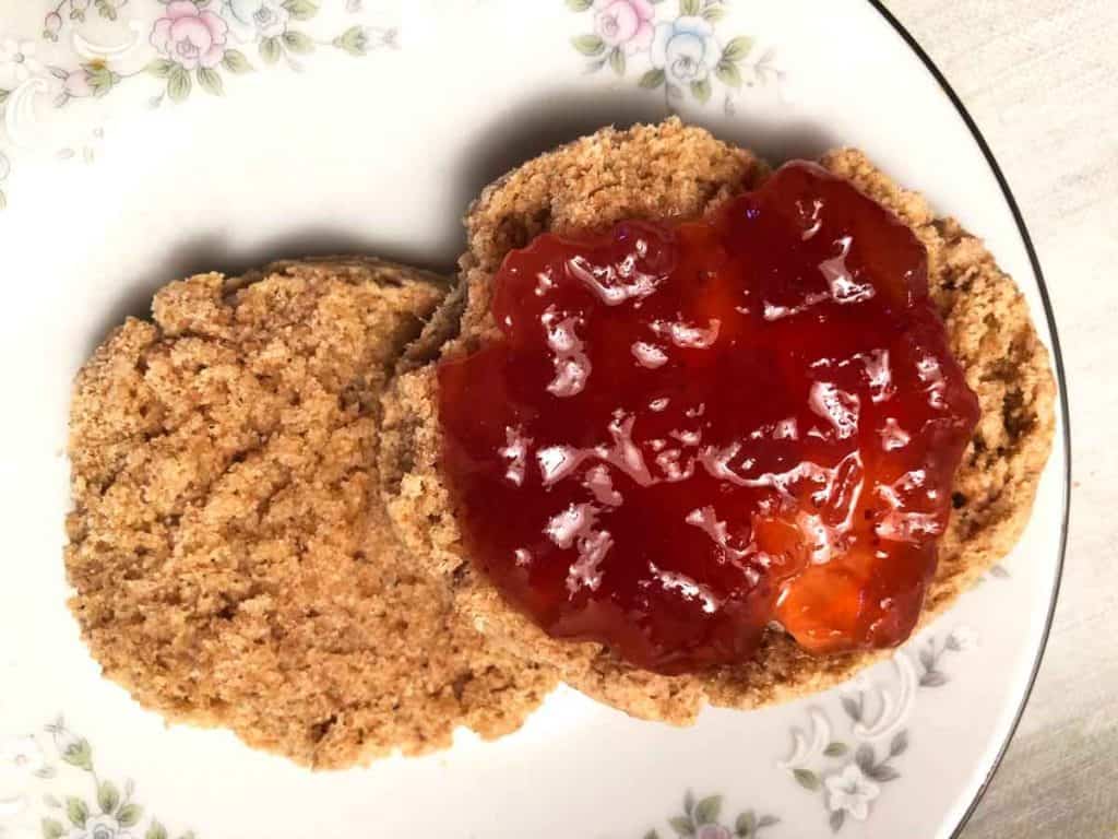 A whole wheat einkorn biscuit topped with strawberry jam is on a floral dish.