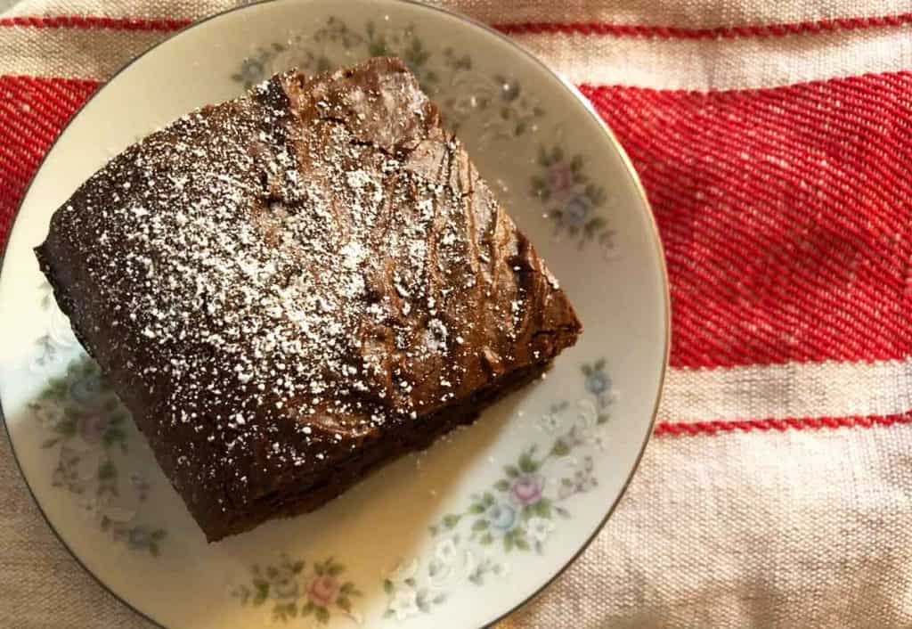 Einkorn gingerbread sprinkled with powdered sugar is served on a floral dish that is on top of a red grain sack towel. 