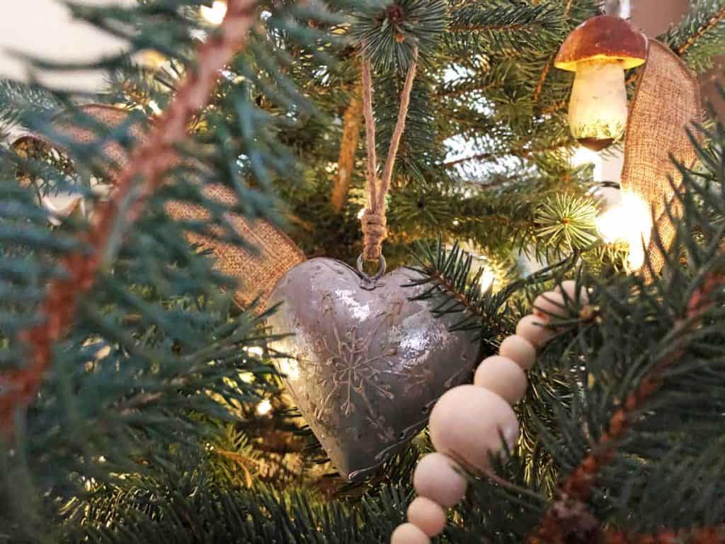 A heart ornament is on a live Christmas tree decorated with wooden beads, burlap, and other nature-inspired decor.