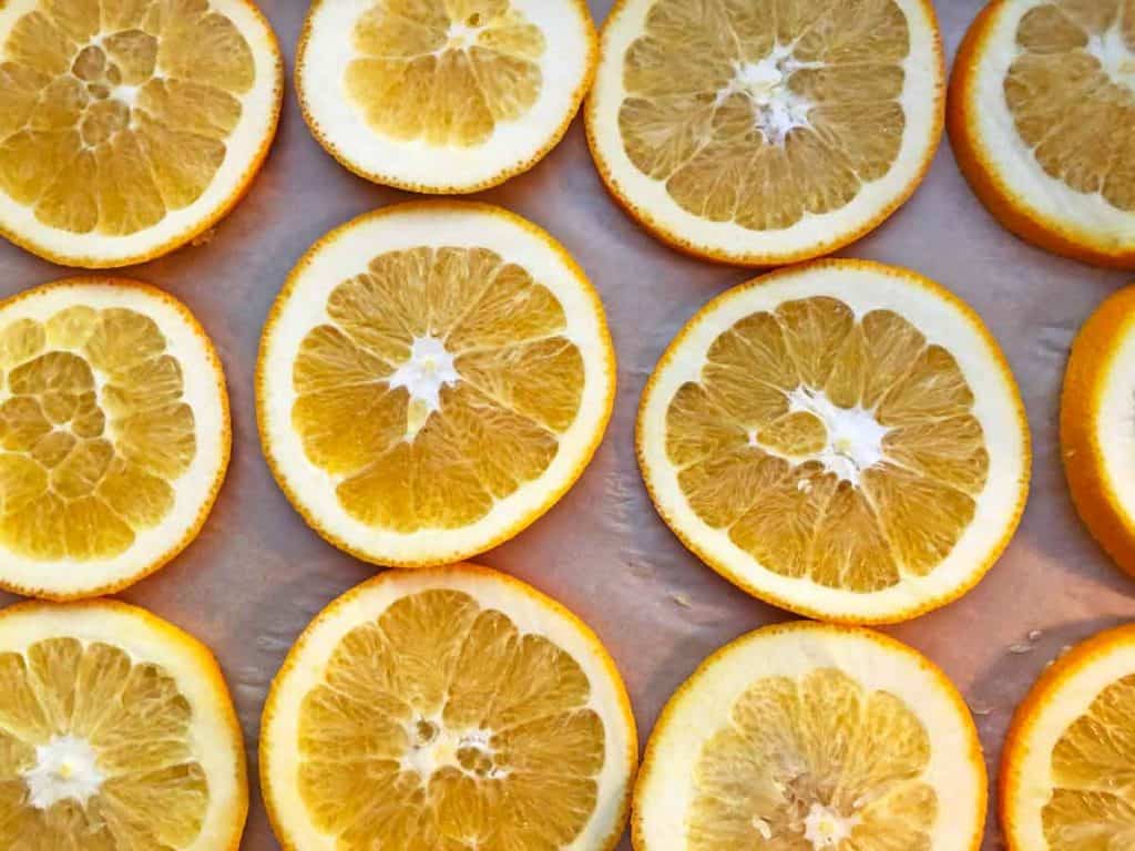 Orange slices are on a cookie sheet lined with parchment paper.