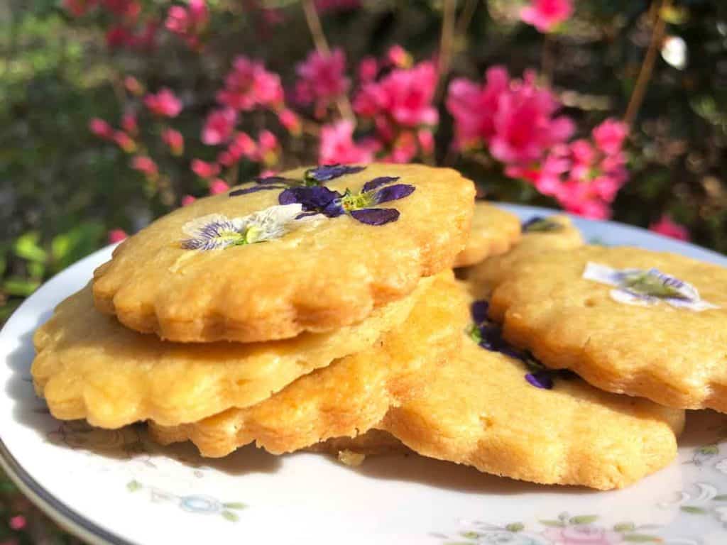 Einkorn shortbread cookies decorated with edible flowers in front of a pink azalea bush. 