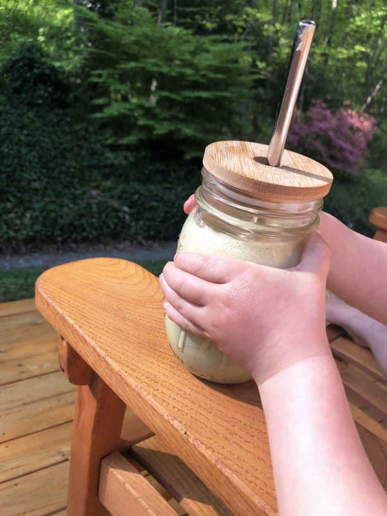A child holds a green smoothie in a wooden rocking chair.