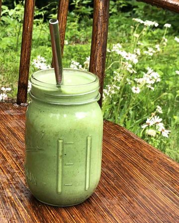 A green smoothie is on a bench beside wildflowers.