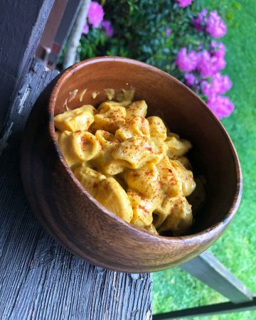 A wooden bowl is filled with sweet potato vegan cheese sauce pasta.