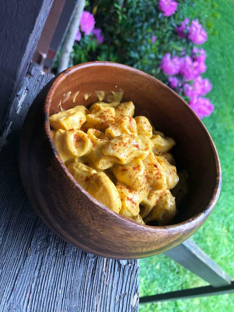 Sweet potato dairy-free cheese sauce with pasta in a wooden bowl outdoors in front of pink flowers.
