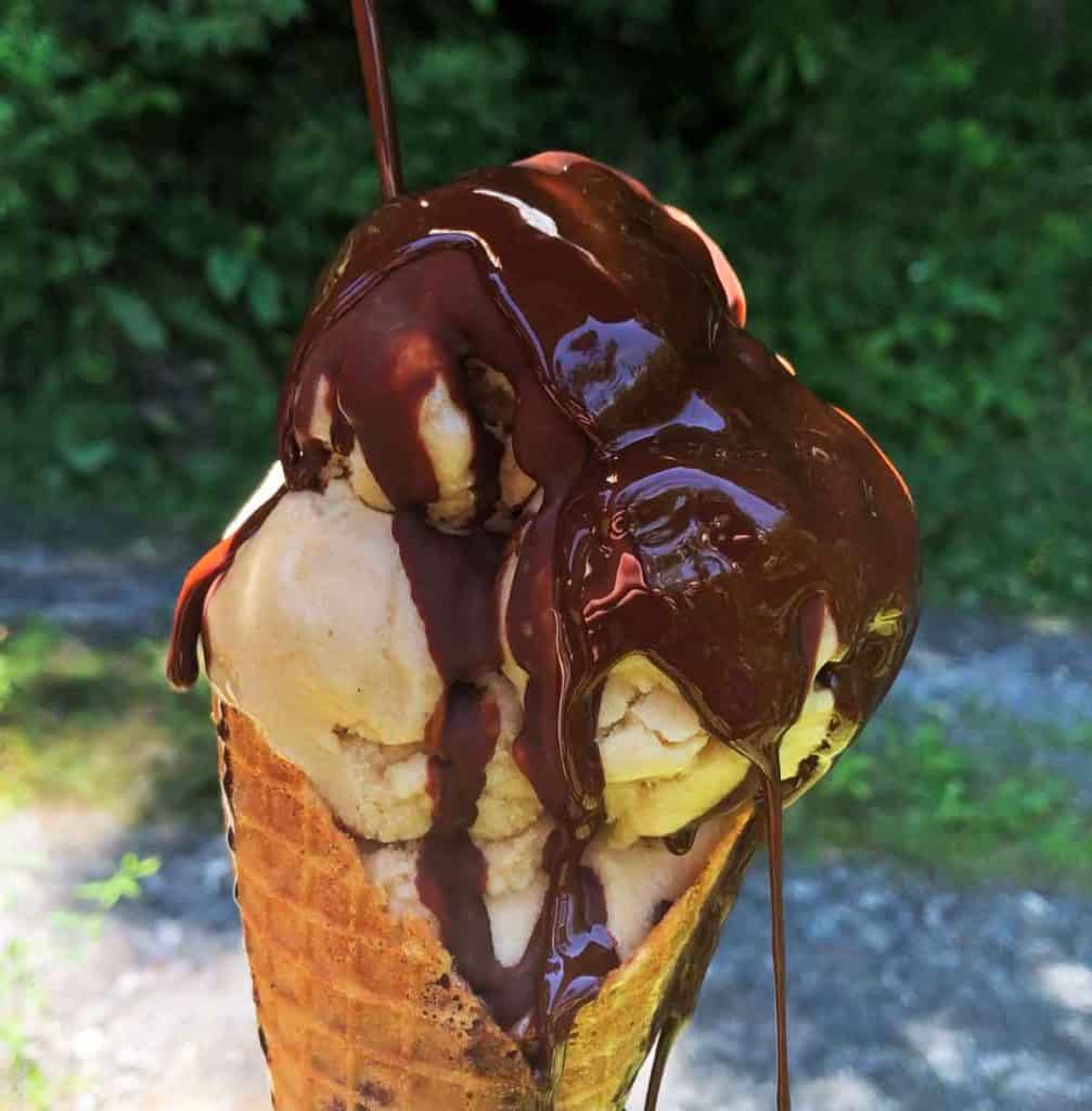 Homemade magic shell is poured over a cone of vegan vanilla ice cream outdoors.