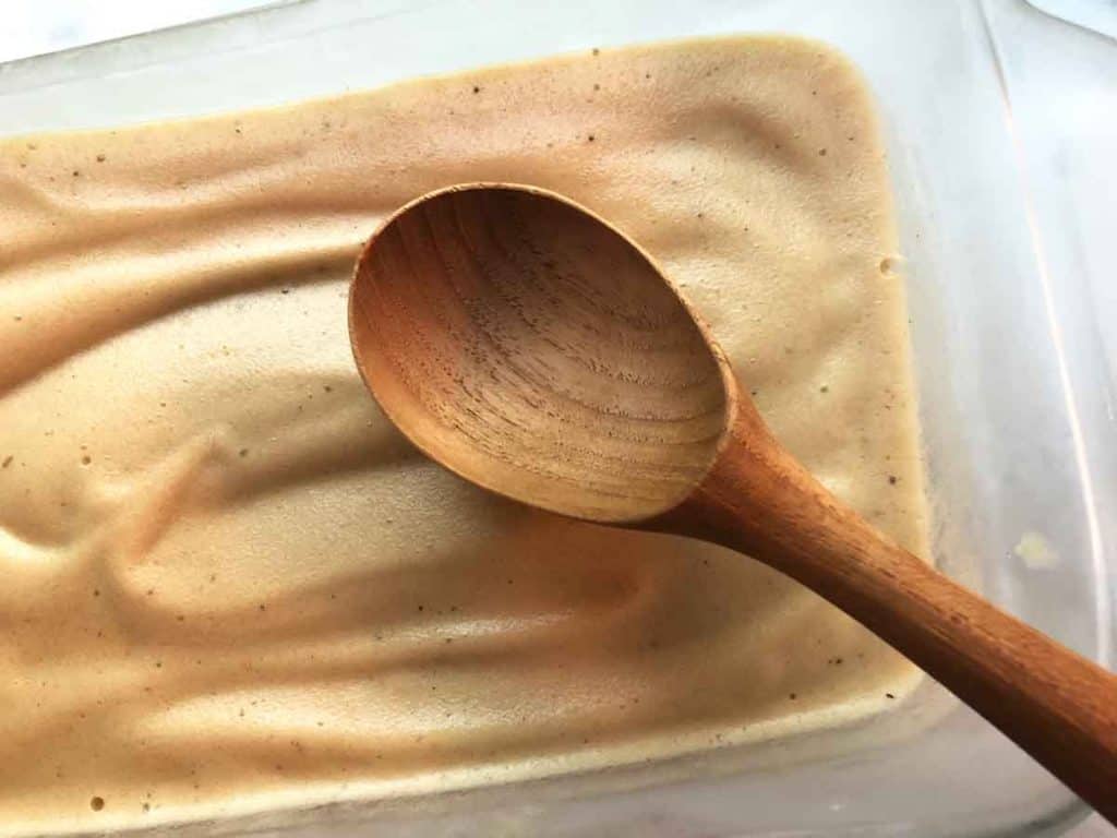Vegan nice cream is in a glass bread loaf pan. A wooden ice cream scoop rests on it. 