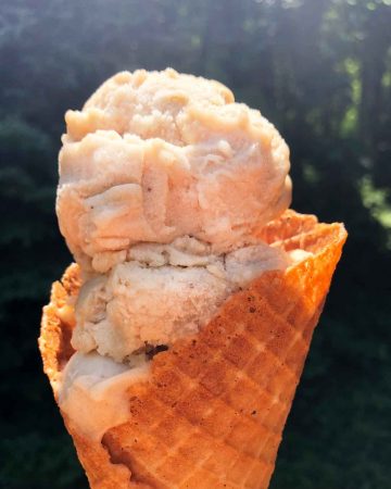 Vegan vanilla ice cream scoops are in a waffle cone outdoors.