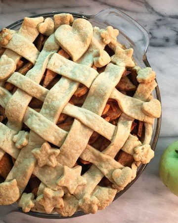 Einkorn apple pie with a lattice crust on a marble countertop beside a fresh picked green apple.