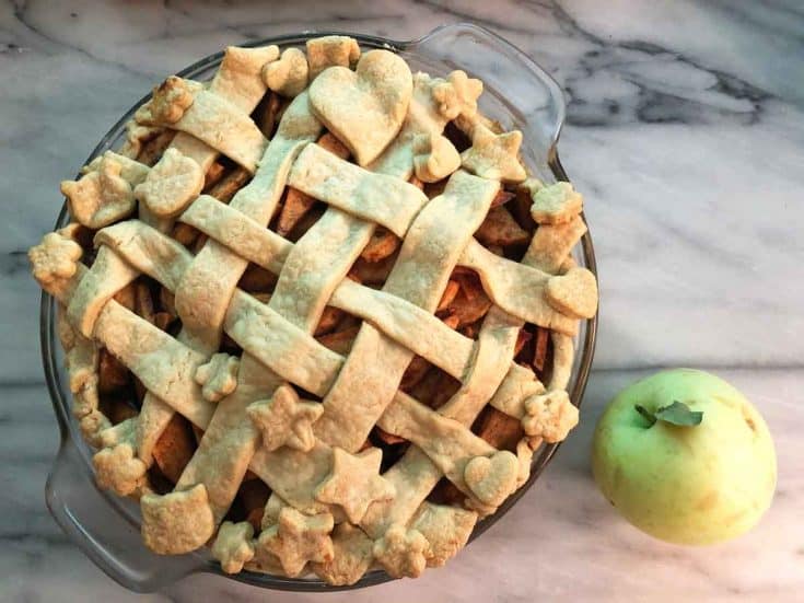 Einkorn apple pie with a lattice crust on a marble countertop beside a fresh picked green apple.